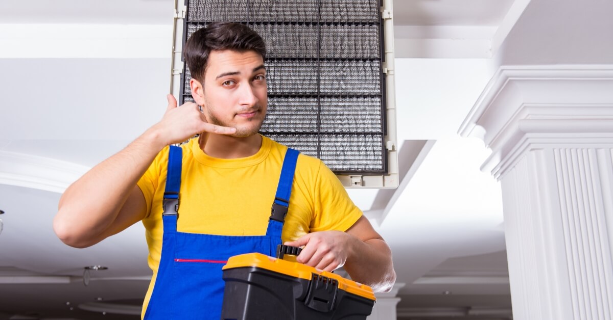 Man Repairing Air Conditioning unit & showing telephone gesture